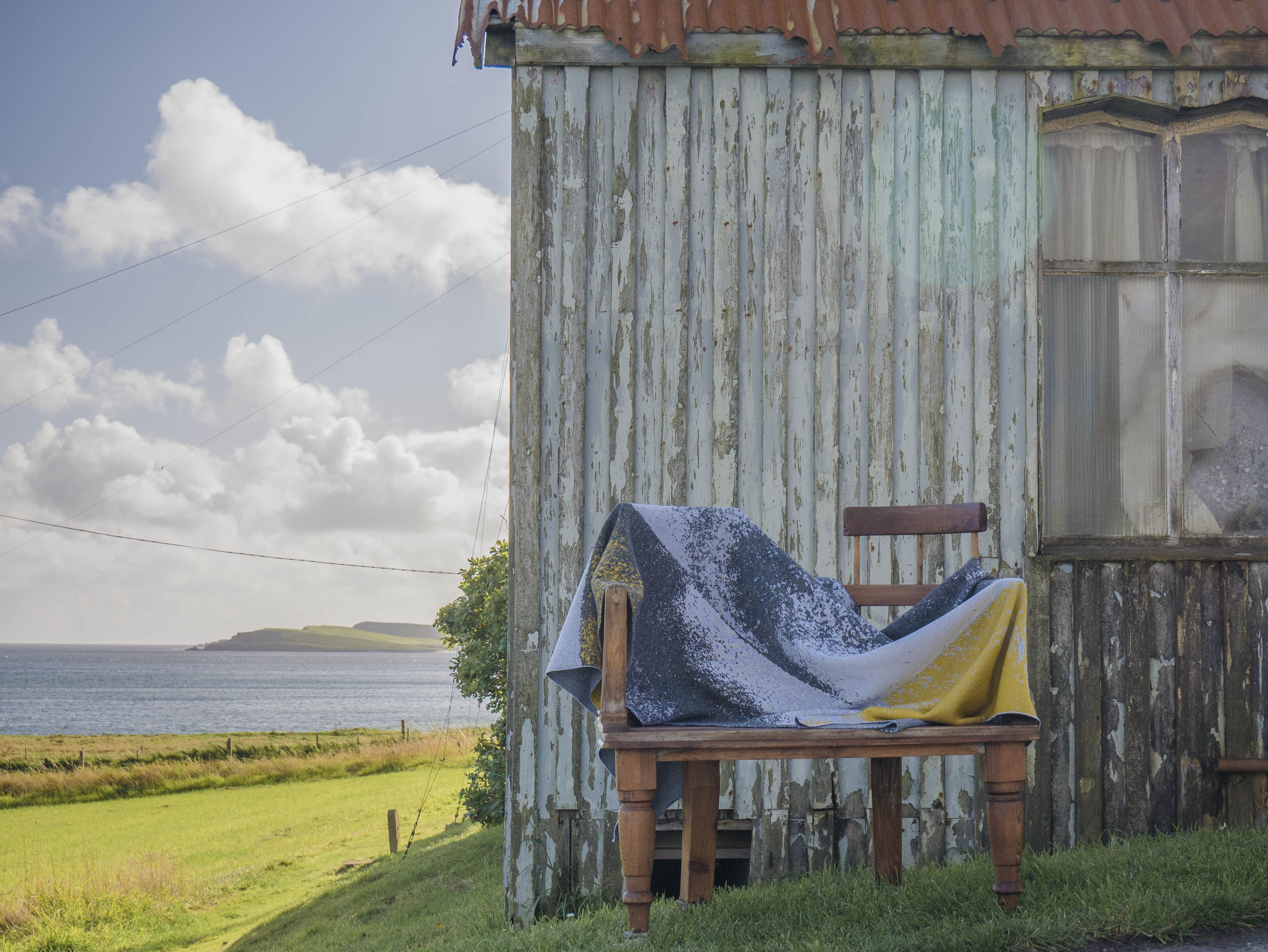 Haar Shetland blanket on a Shetland love seat, outside the Gospel Hall, Hoswick. View to the sea behind. Blanket knitted in greys and yellows