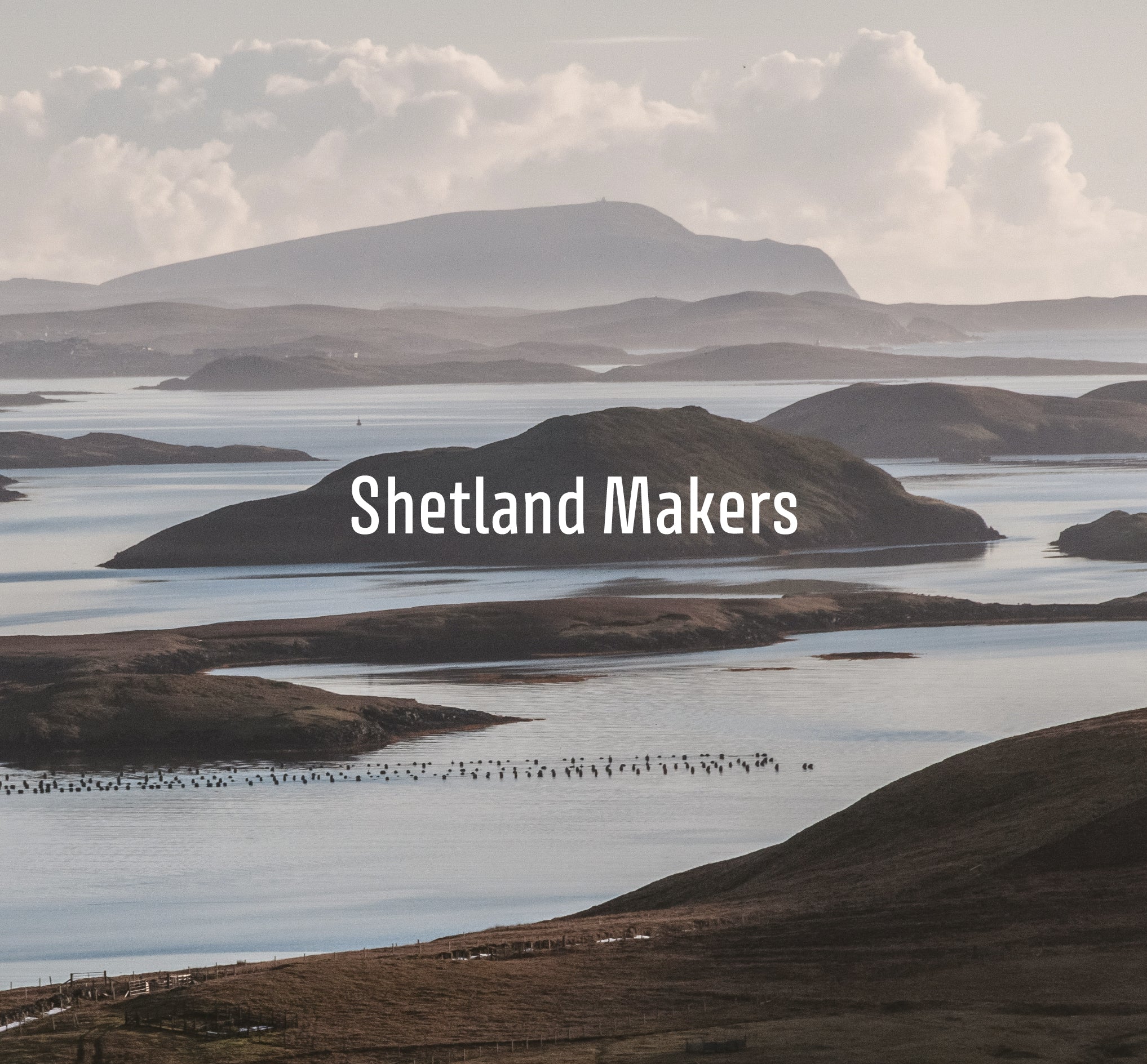 A Shetland sea and landscape of small islands in a sea Loch. A headland rises behind. Muted, hazy colour with glowing reflections on the sea. In white type, on one of the islands 'Shetland Makers'.