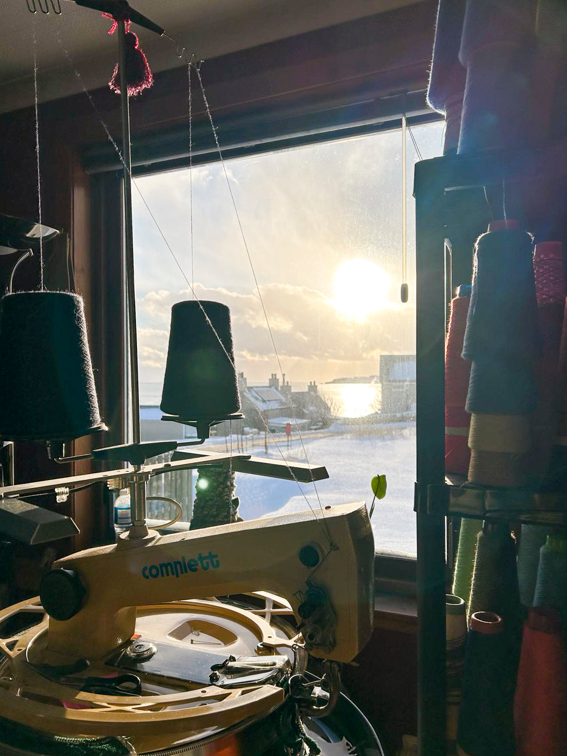 In the knitwear studio at Nielanell, Shetland. A view out with linking machine in the foreground to the snow covered gardens and sea beyond. Soft low winter light.