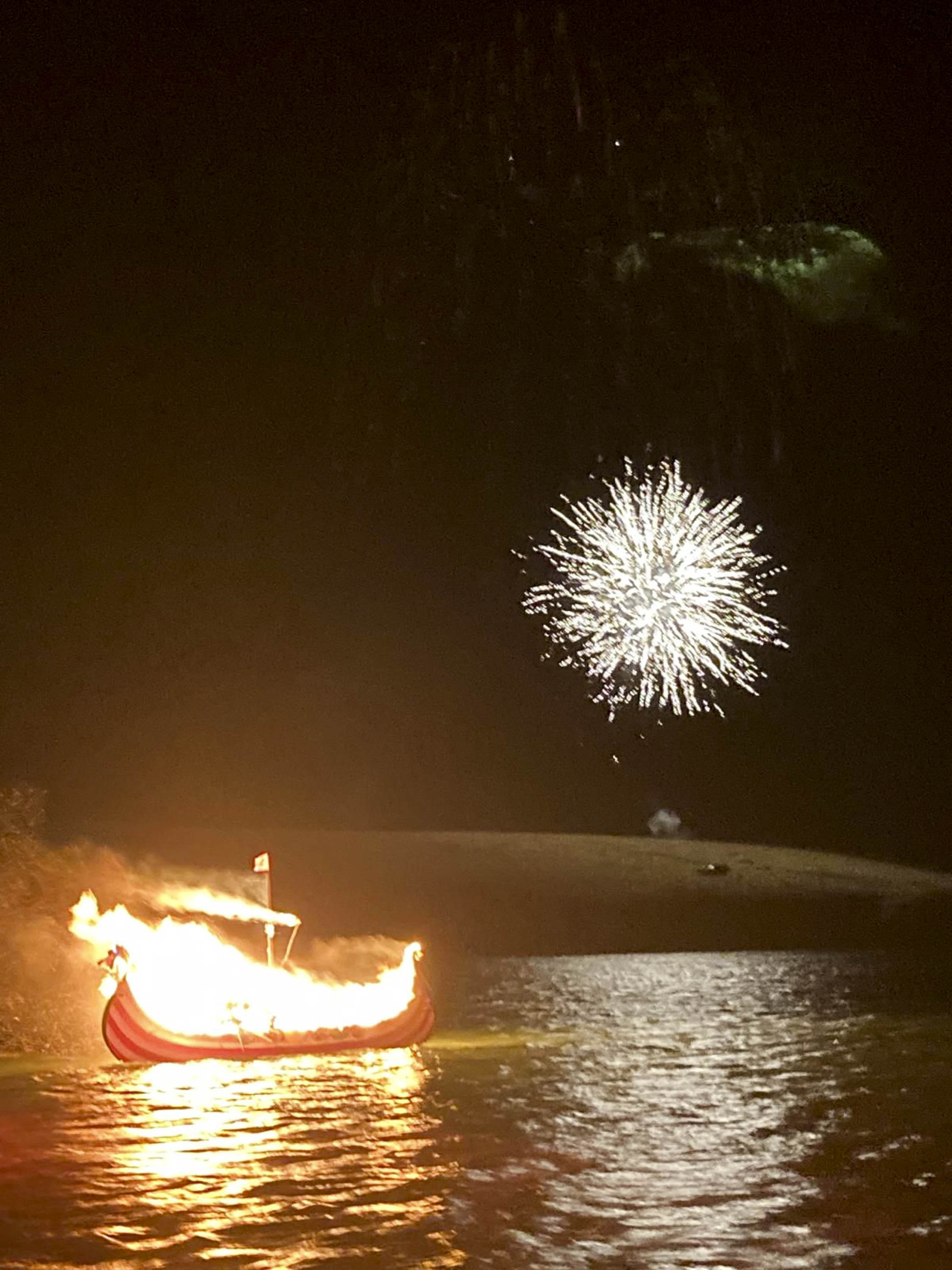 Just off the sea at Scousburgh, Shetland, the viking galley is ablaze as it floats at sea. A firework lights up the sky