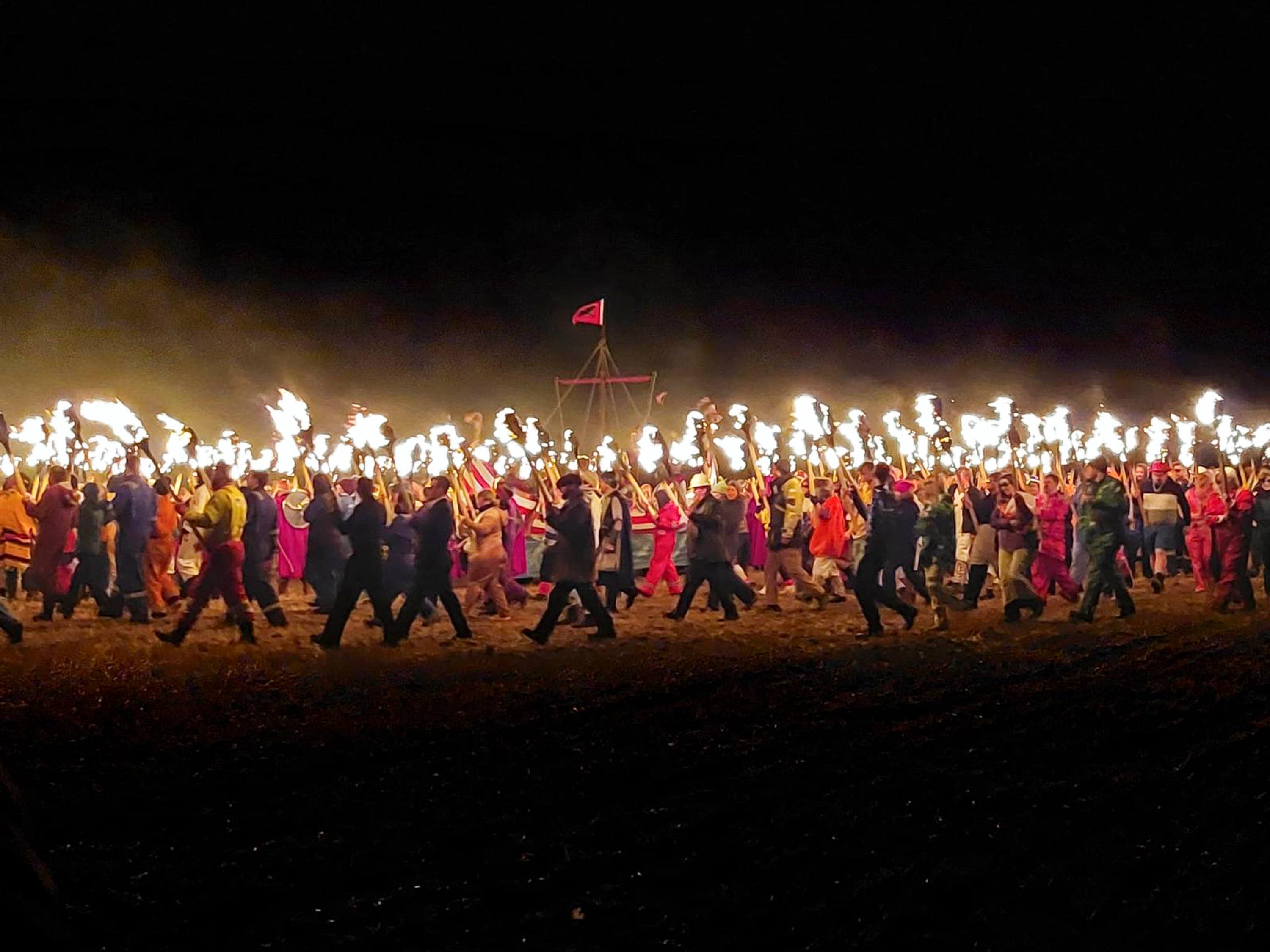 On the beach at Scousburgh, guizers holding flaming torches circle the replica viking ship at South Mainland Up Helly Aa