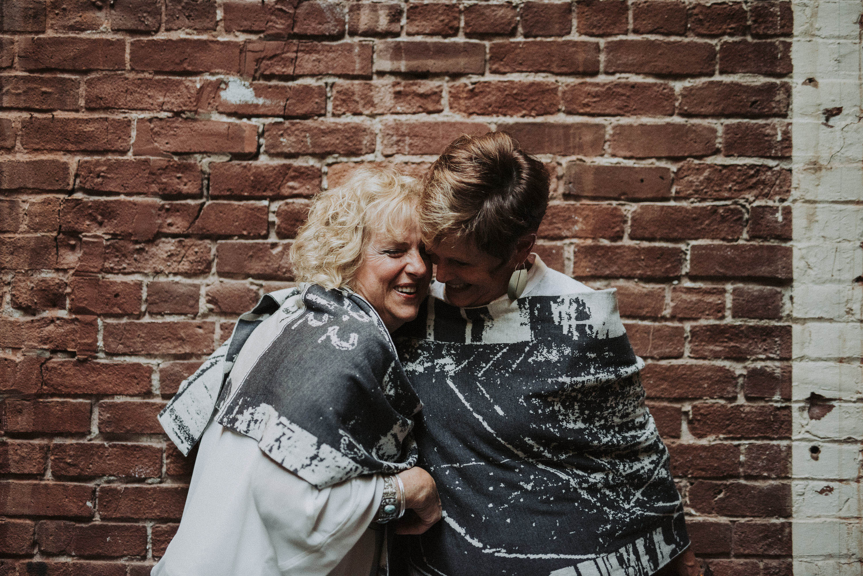 Two women hug, they are both wearing Byre contemporary knitwear in charcoal and stone white