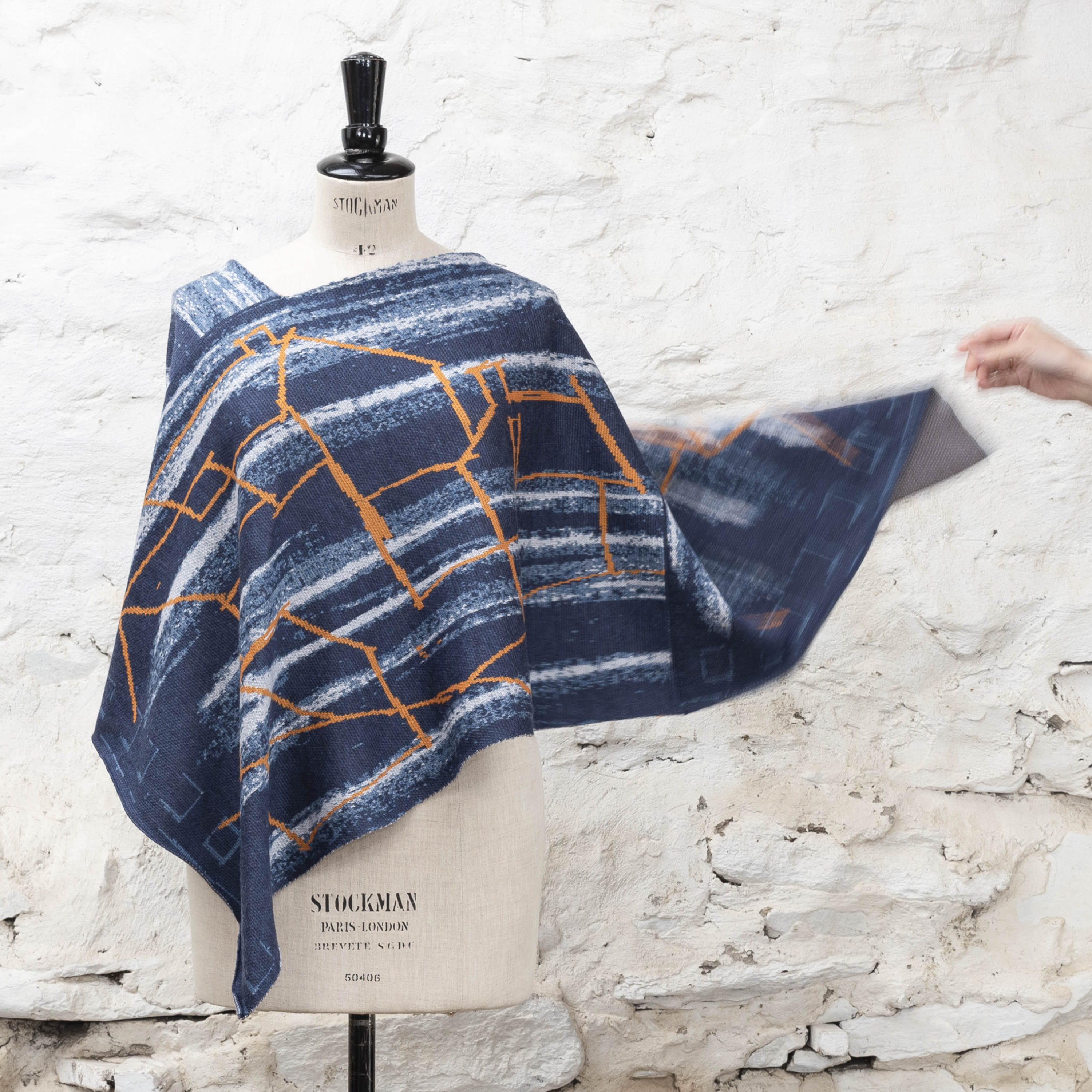 An edgy designer knitwear cape, made in Scotland. Abstract patterning in orange and blue, knitted in extra-fine merino