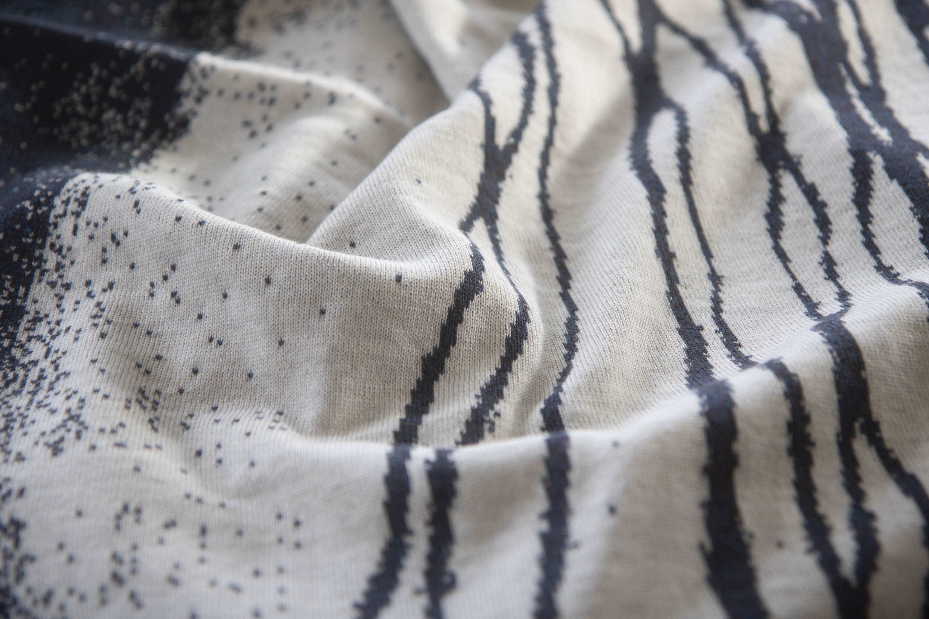 detail of knitted textile in deep navy and off-white with flowing lines and speckles.