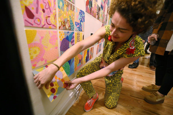 The artist pulls a mini painting off the wall
