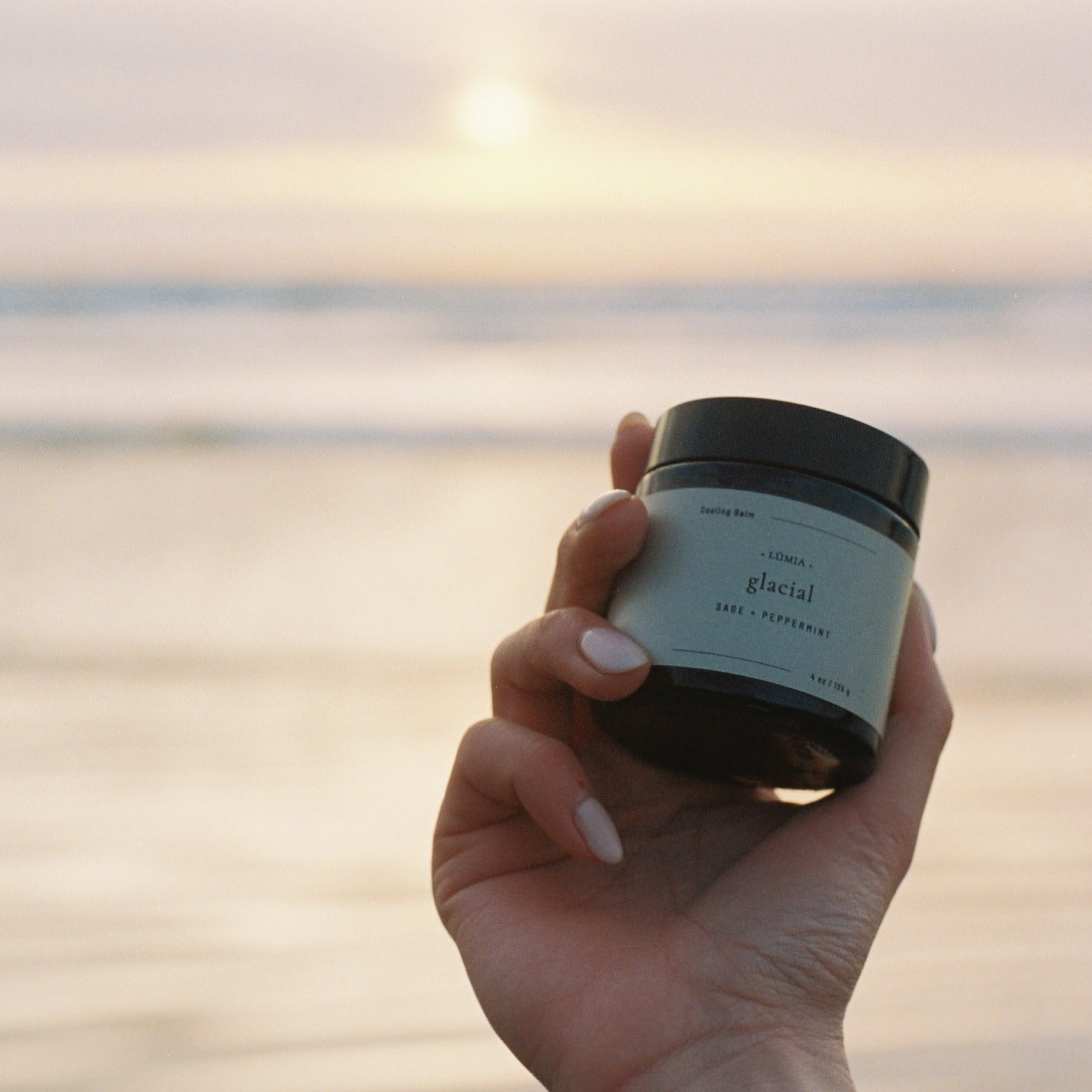 Waterless Skincare, Glacial Cooling Balm held out over ocean sunset