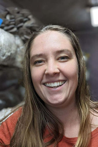 a smiling woman in front of a mushroom grow room