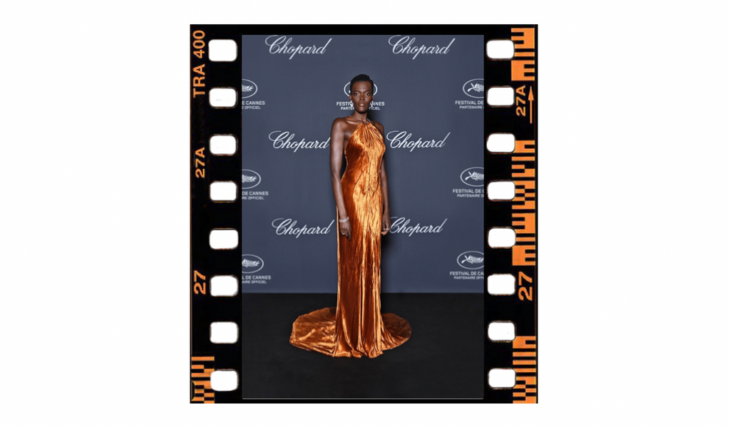 Actress Sheila Atim is standing on the step and repeat for the Choppard red carpet. She is wearing a bronze velvet halter neck gown.