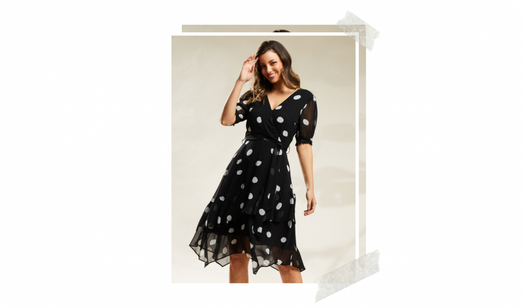 Model is posing in a black dress with a milk coloured dots pattern. The dress has 3/4 length sleeves and a handkerchief hemline. 