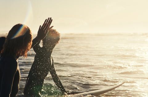 surfers giving each other hi 5 in sunset waters