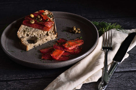 Tranches de gravlax de saumon dans une assiette grise sur fond noir