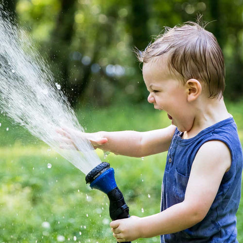 A very happy boy plays with a water sprinkler on a summer day.