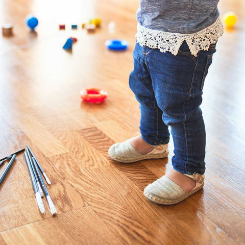 A child is in kindergarten playing in a large room and has a pair of sandals on his feet.