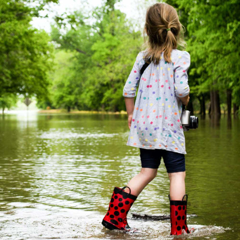 En flicka står i en stor vattenpöl med ett par färglada gummistövlar på fötterna.