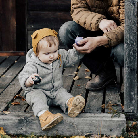 En liten flicka sitter ner utomhus på hösten i ett par lätta barnkängor.