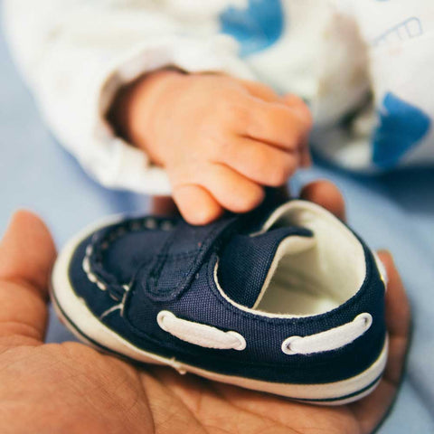 Et lille barn, en baby, holder sin hånd på et par børnesko ved hjælp af velcro til at tage dem på.