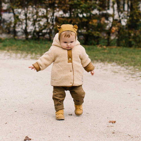 A cute kid walks in a pair of children's shoes along a gravel path that is a learn-to-walk type of shoe.