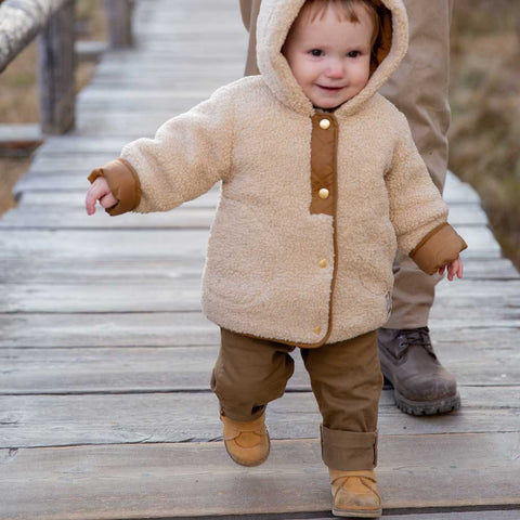 A happy child walks on a bridge with staggered steps and balances his progress in a pair of trainers.