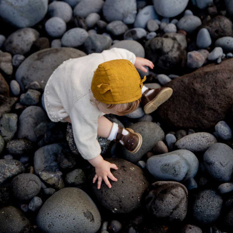 Et barn sidder på mørke sten og leger med et par kondisko på fødderne.