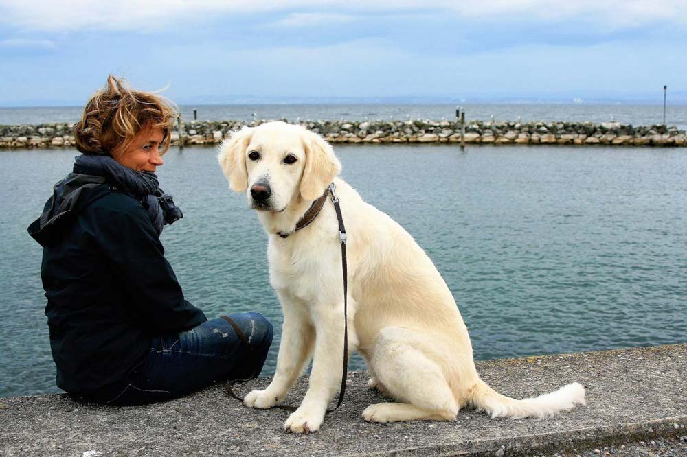 A woman and a white dog sitting by the water