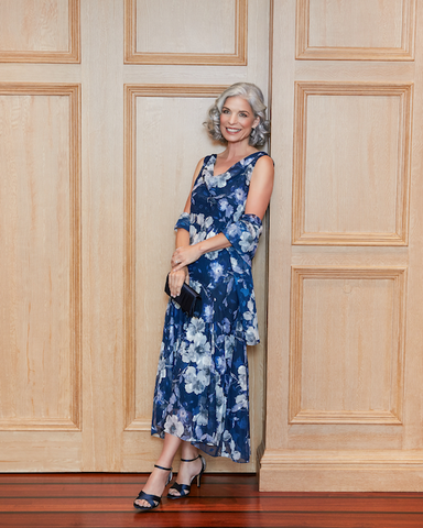 Woman leaning against door in a navy blue floral high-low formal dress