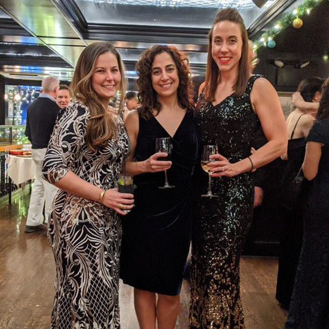 Image of three women in festive formal dresses, enjoying a festive party