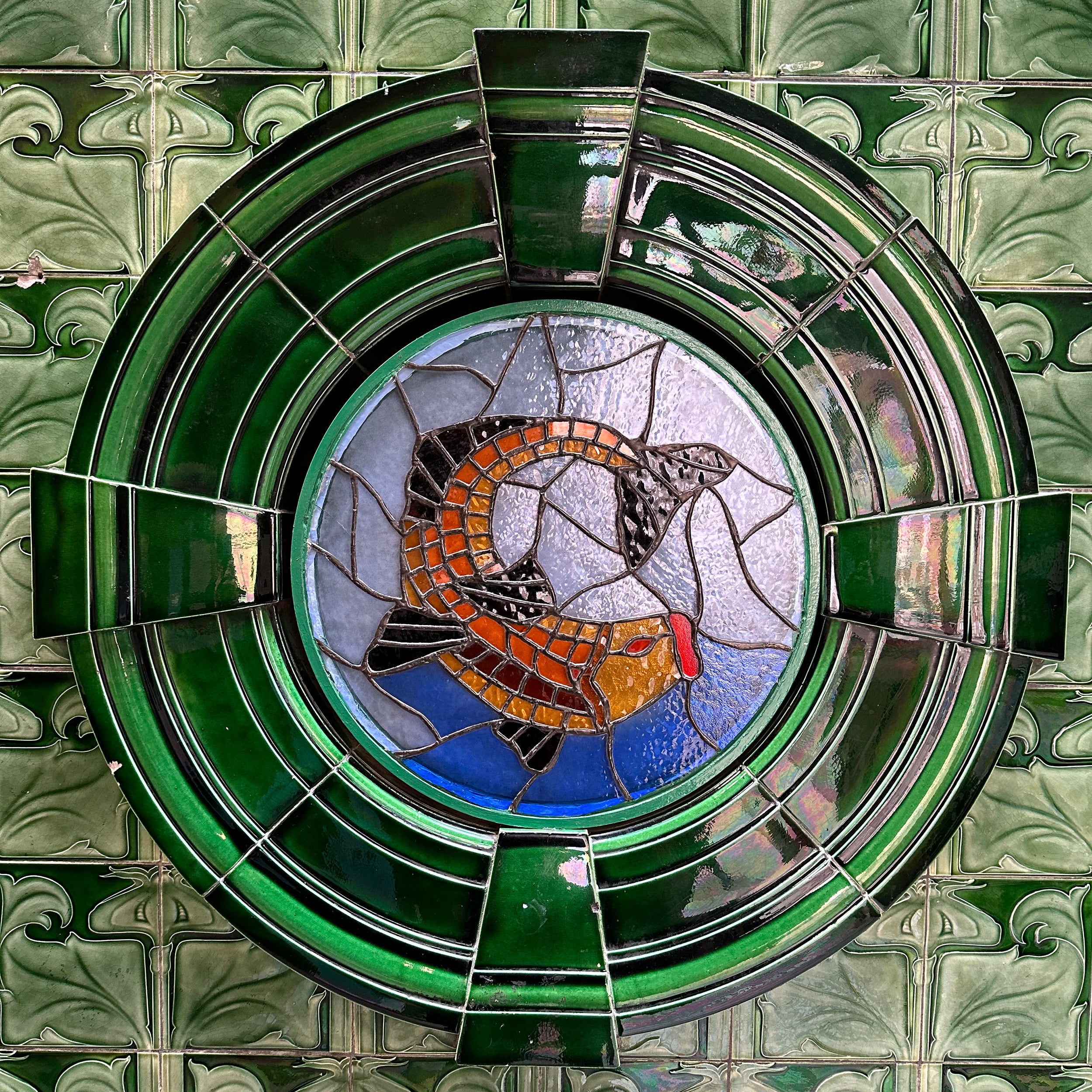 Circular stained glass window of a fish surrounded by green tiles