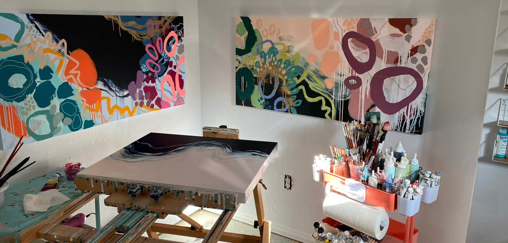 Artist studio with paintings on the wall, a cart of supplies, and an easel