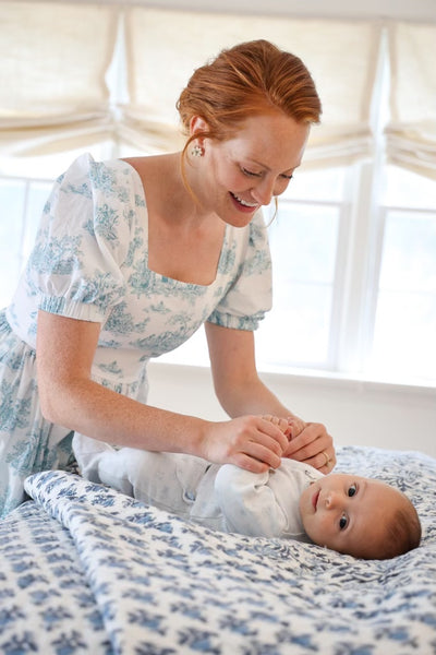 Therese wearing a Lan Midi Dress with nursing zippers in Blue La Mere Toile while playing with her baby boy on the bed