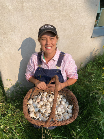 Woman holding a basket of garlic bulbs standing beside a house