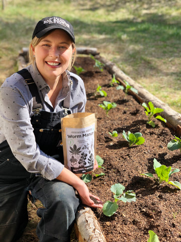 Woman holding open bag of worm manure in front of an outdoor garden