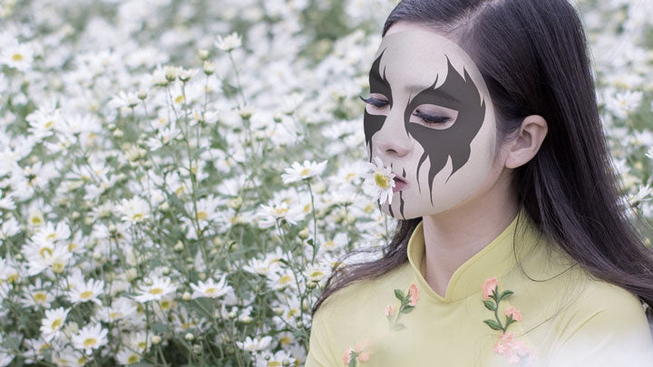 A girl wearing corpse paint smelling flowers