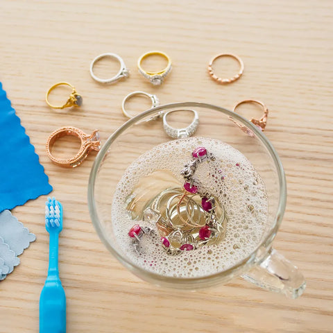 Cleaning diamond gold engagement ring with soap water at home to remove any dirt and debris.