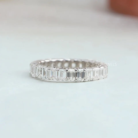 Emerald diamond cut eternity wedding band with U shaped prong settings and white gold material that increases the natural appearance of colorless diamond.