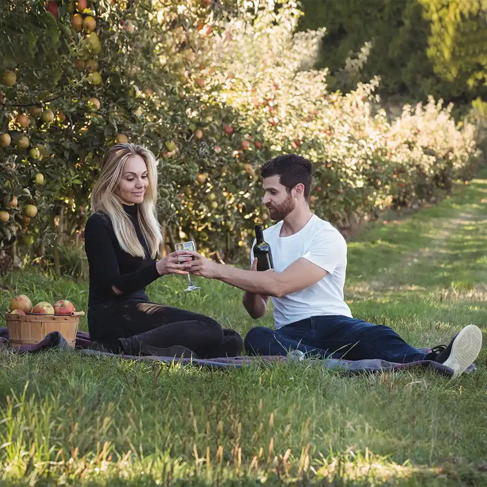 Mann bietet seiner Partnerin im Garten Champagner als Teil eines Heiratsantrags an