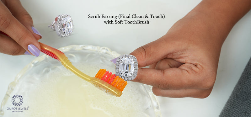 [ Using a soft toothbrush to gently scrub a diamond earring for the final cleaning touch, with a focus on detail and care]-[ouros jewels]