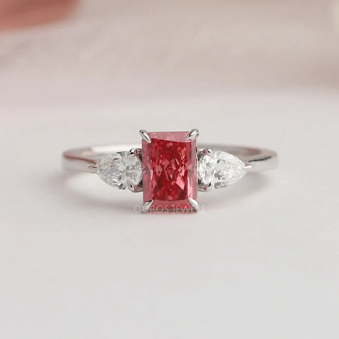 1.10 carat weighted pink radiant cut lab grown three-stone engagement ring with pear shape and round cut diamonds.