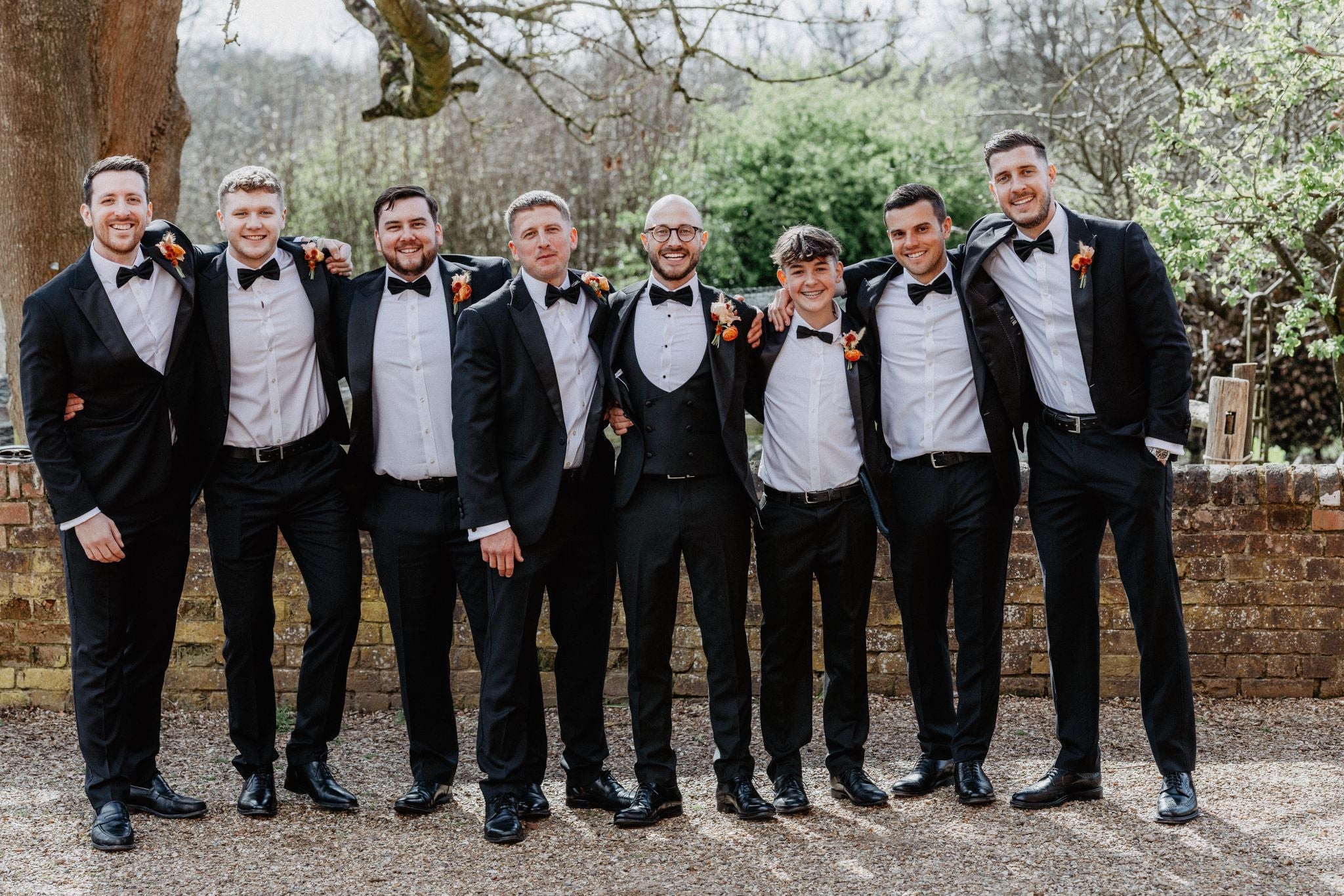 Groom and groomsmen in black tie with matching orange flowers