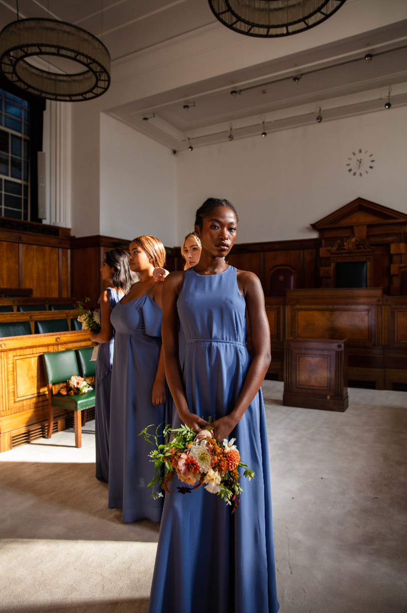 Four girls standing in the council chamber at Town Hall Hotel, all in dusky blue bridesmaids dresses holding bouquets of flowers.