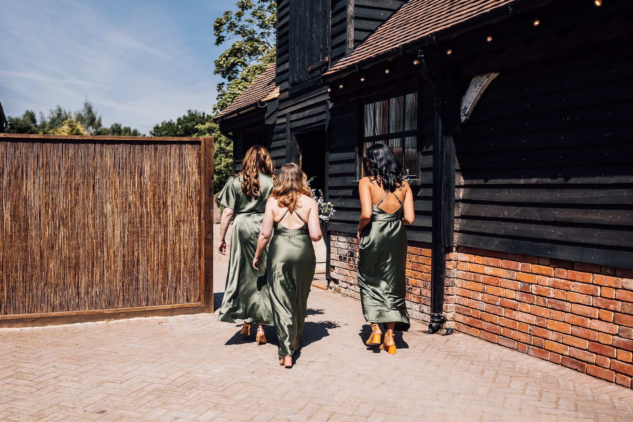 Tre flickor går utanför Stanlake Park Vineyards bröllopslokal i Twyford, klädda i gröna satinklänningar för brudtärnor med korsrygg.