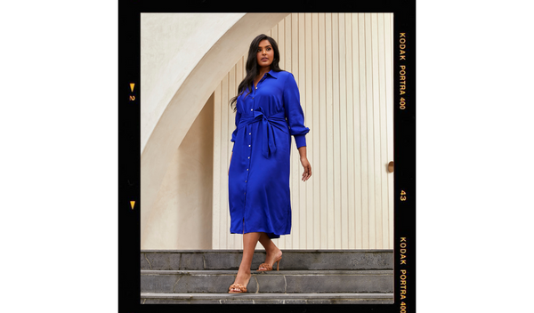 Pictured: Model walking down stairs wearing the Monaco Tie Dress - a cobalt blue long sleeve midi dress.