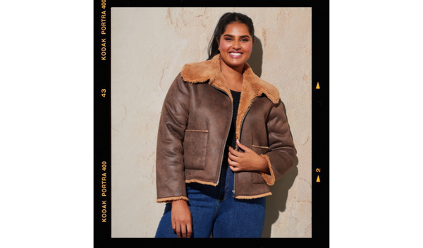 Pictured: Model posing and smiling for the camera in the comfy Lenny Jacket by Estelle. The jacket is chocolate coloured and lined with a tobacco coloured faux shearling. 