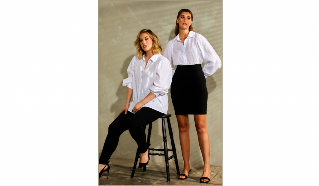 Pictured: Two female curve models standing side by side. The one on the left is wearing black tight fit pants with The Mercer Top - A white shirt. The model on the right is wearing the same women's white shirt, but with a short black skirt.
