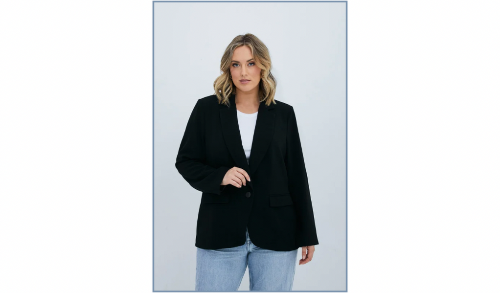 Pictured: Model Jess wearing light wash jeans, she is wearing the Megan Blazer. The blazer is a women's plus size black blazer with a single fastening button at the front.