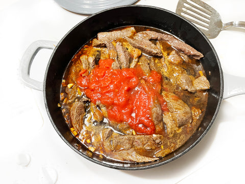 crushed tomatoes and meat cooking in grey saute skillet