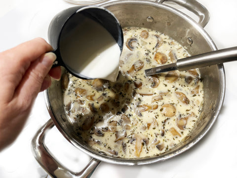 adding cream to mushroom soup in stainless steel stockpot