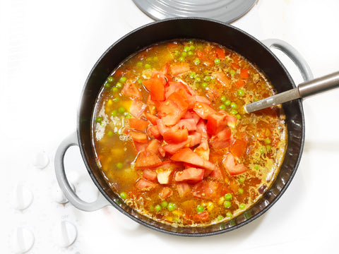 adding tomatoes to quinoa stew in dutch oven