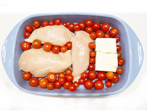 tomatoes around chicken and feta cheese in glacier blue rectangular bakeware