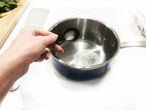 adding salt to stripes saucepan for orzo pasta salad