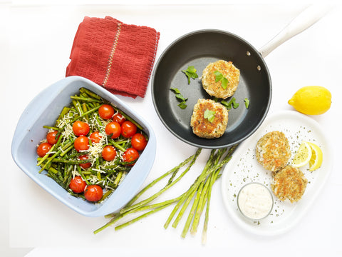 CRAB CAKES PLATED WITH aspargus and tomatoes in square ceramic baker